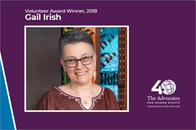 [ai] A portrait of Gail Irish, a woman with short gray hair wearing glasses and a brown blouse, smiling in front of a colorful patterned background. The image includes text indicating she is the Volunteer Award Winner for 2018.